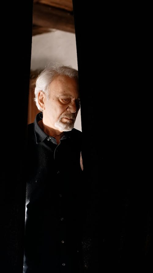 A Sad Elderly Man Behind a Black Curtain
