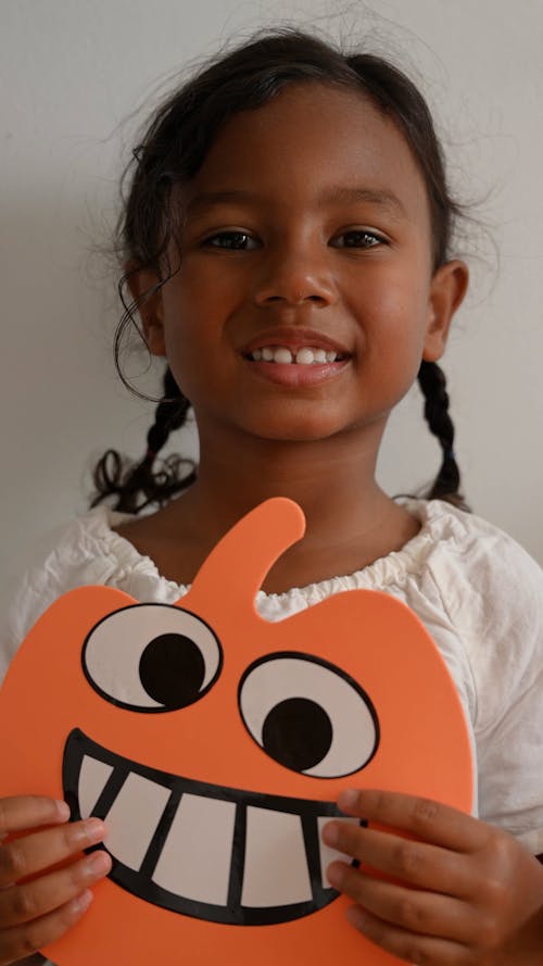 Young girl holding toy pumpkin made of cardboard