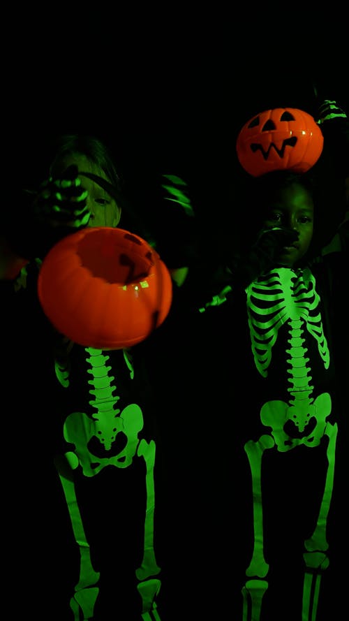 Kids in skeleton costumes holding plastic Halloween pumpkin
