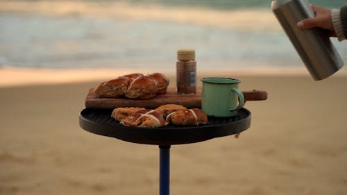 A Person Pouring Coffee into a Mug by the Seaside