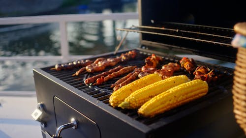 A Person Grilling Meats and Corns