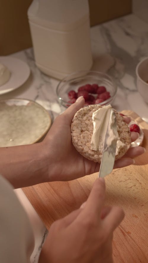 A Person Spreading a Cream on a Bread while Putting Raspberries