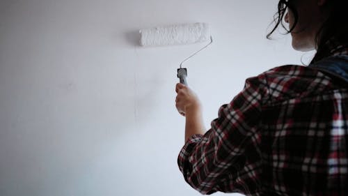 Rear view on woman painting wall with white paint