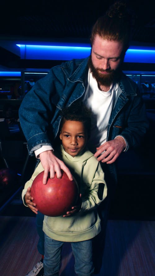 Man helping girl holding bowling ball