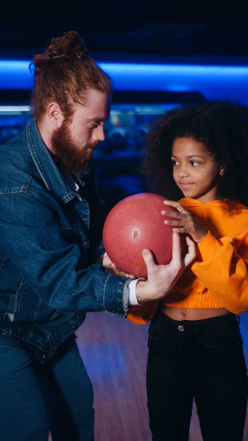 Redhead man instructing curly hair girl in orange sweatshirt